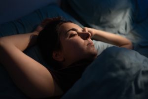 Woman lying awake in bed at night while experiencing discomfort and difficulty sleeping.